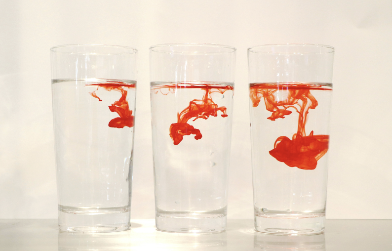 3 glasses of water in front of a white background with drops of Red dye in each of them. 